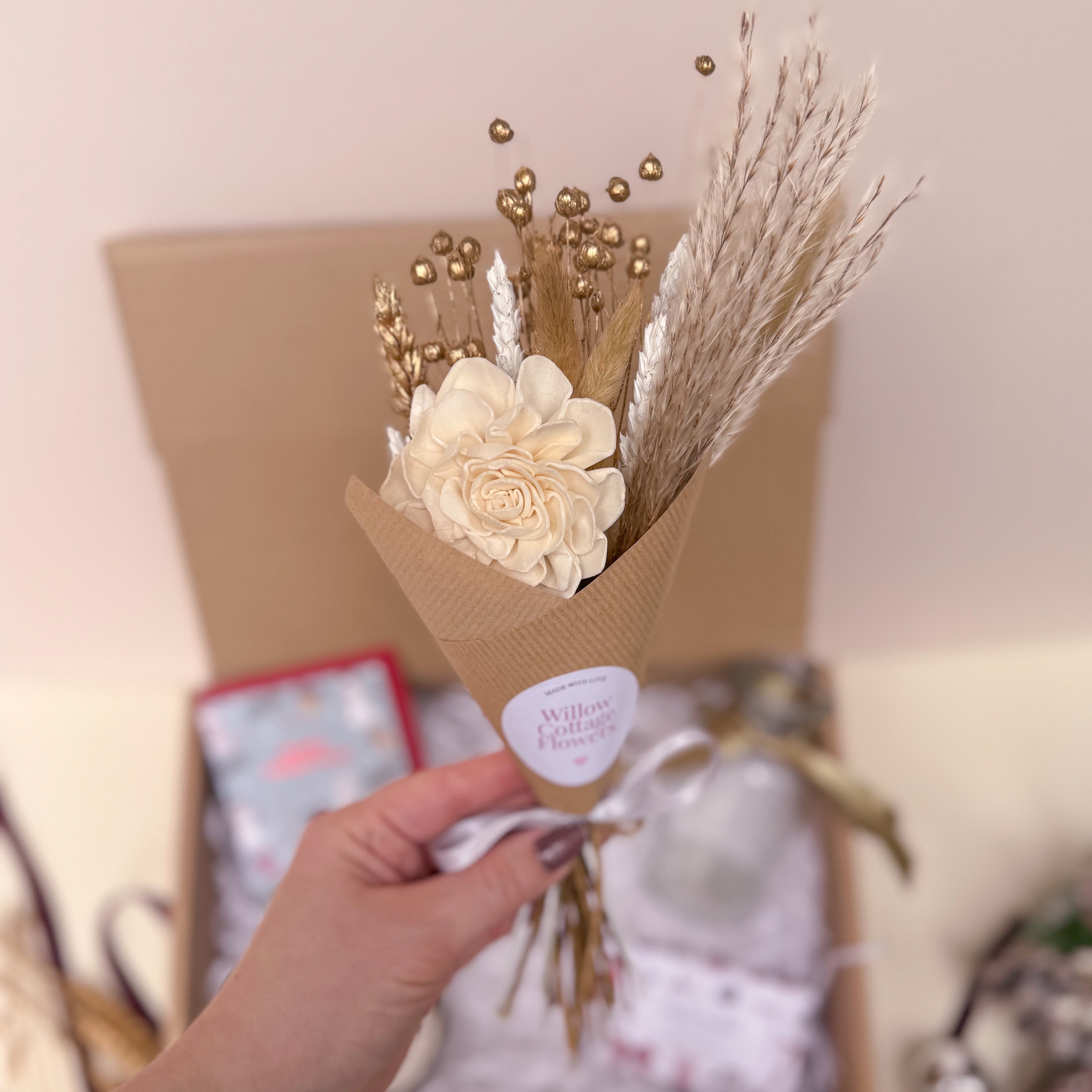 Bouquet of white and gold dried flowers in brown paper held by a hand with a blurred background