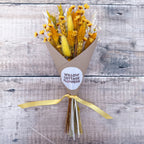 a small bunch of yellow dried flowers wrapped in brown paper against a wooden background