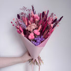 Bouquet of pink and purple flowers held against a light gray background