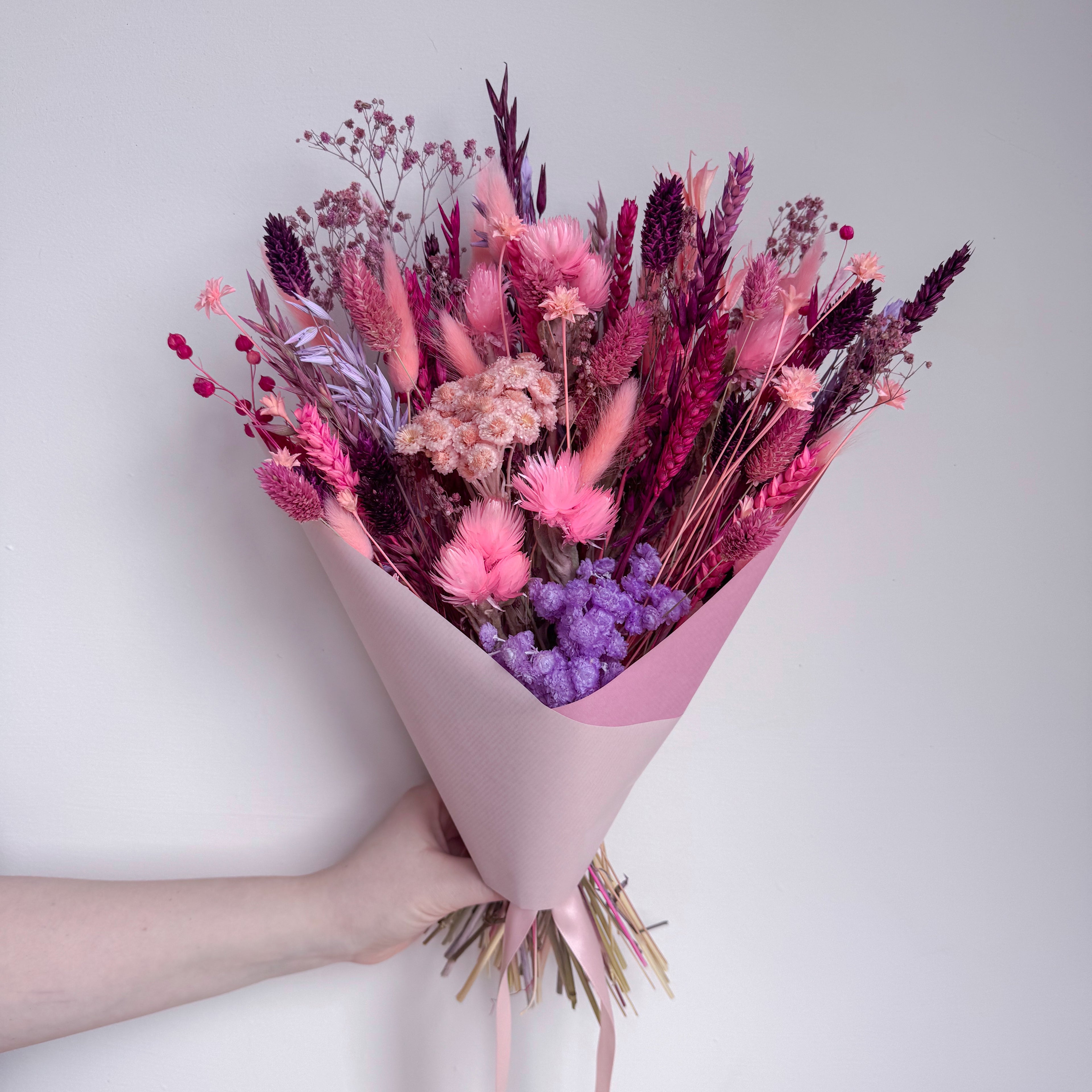 Bouquet of pink and purple flowers held against a light gray background