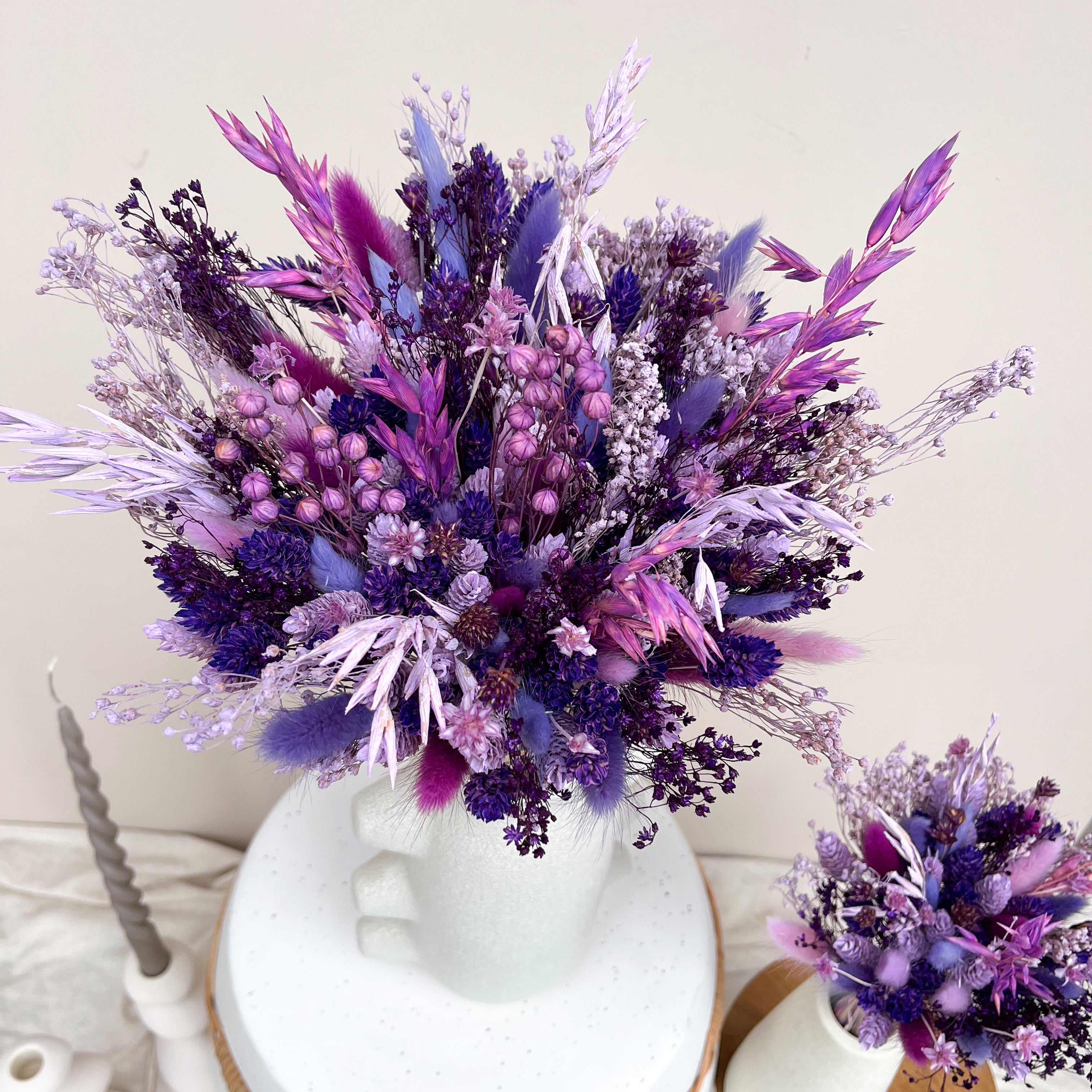 purple dried flower arrangement with oats, bunny tails, phalaris and linum displayed against a white background