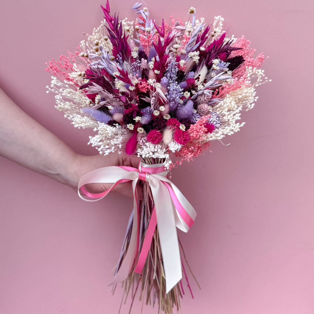Bouquet of flowers with pink and white ribbons against a pink background