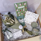 Gift box with various items including a candle, soap, and decorative elements on a light background themed for a housewarming gift