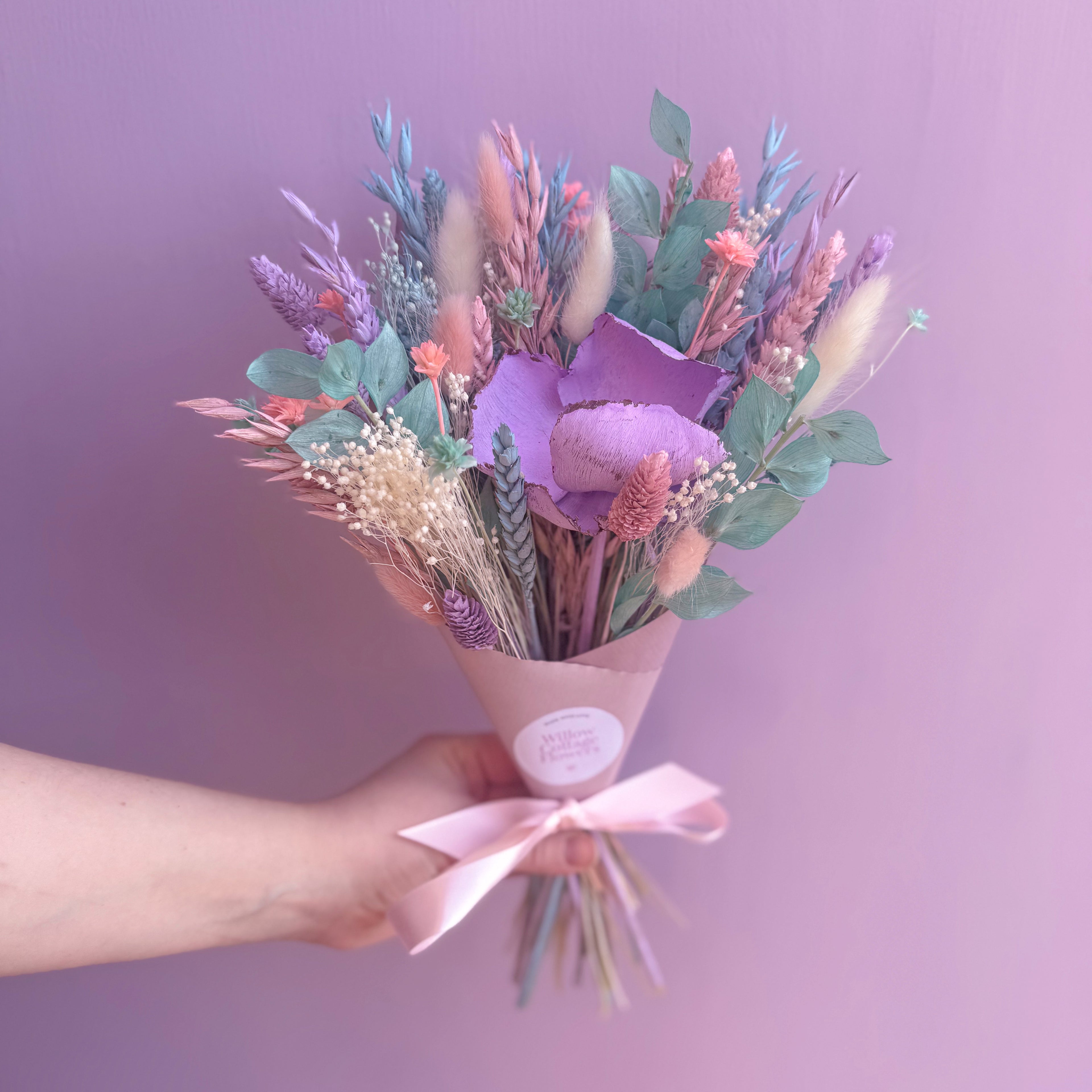 Bouquet of colourful flowers held by a hand against a purple background