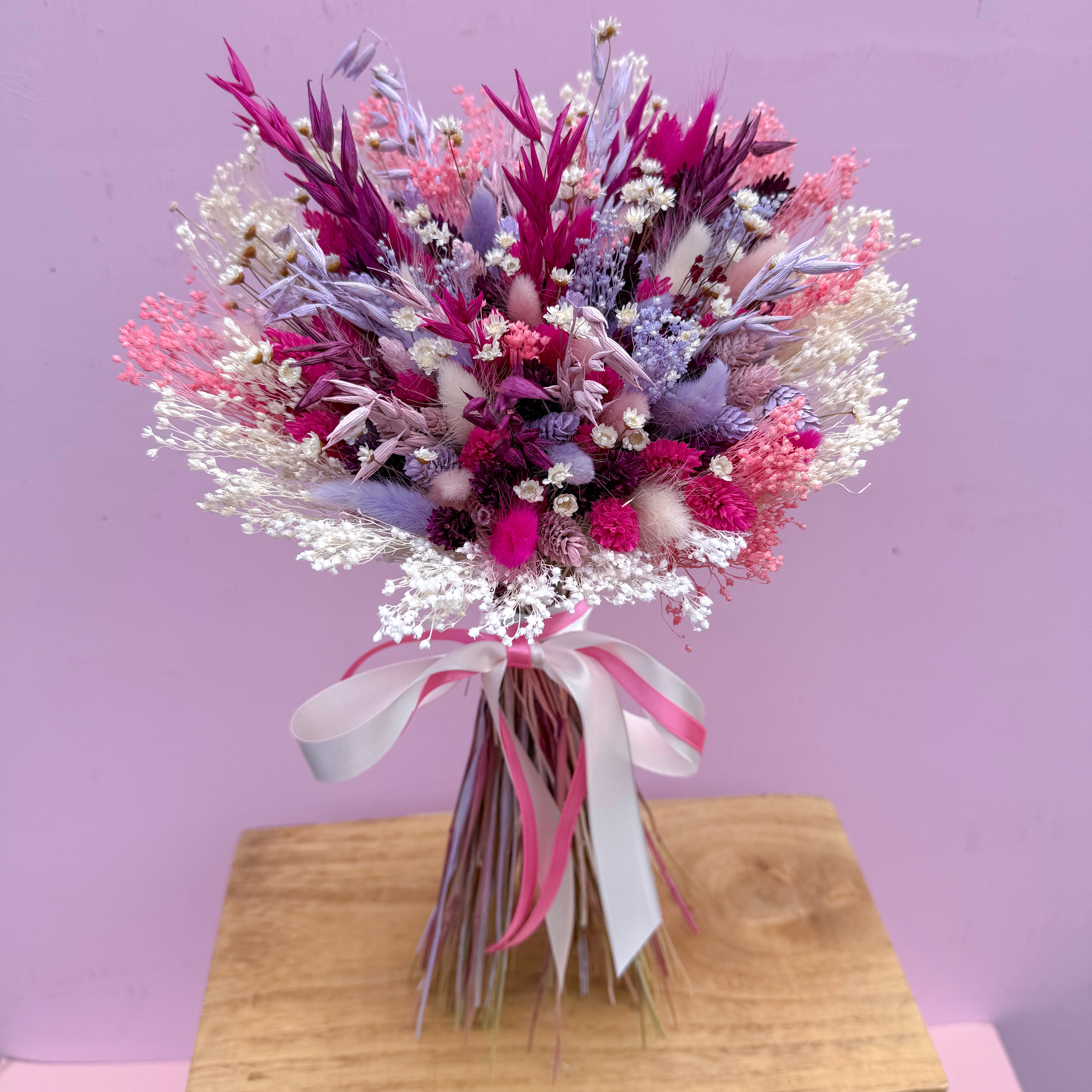 Bouquet of dried flowers with pink and purple tones on a wooden stand against a pink background