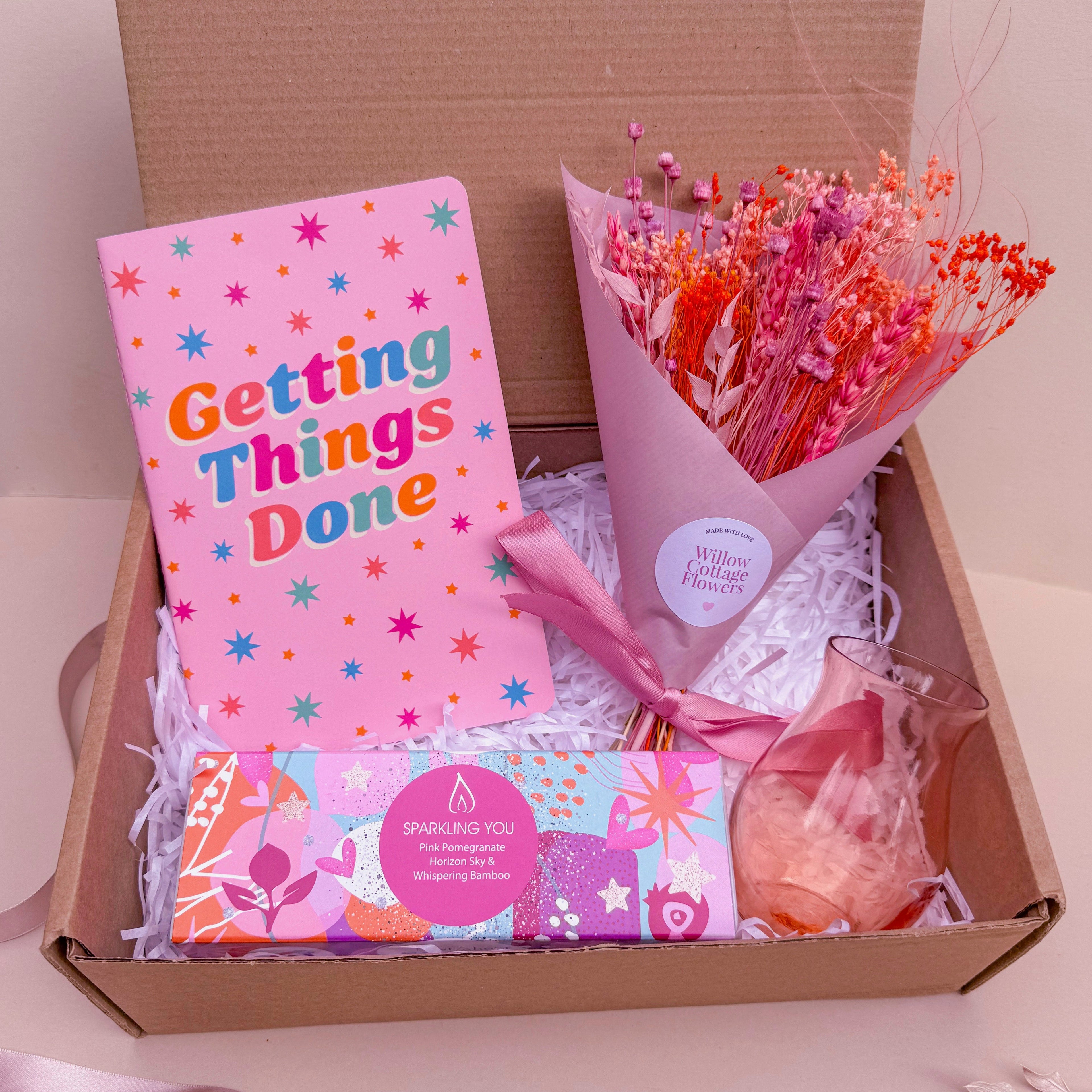 Gift box with 'Getting Things Done' notebook, pink candle, and bouquet of flowers on a light background
