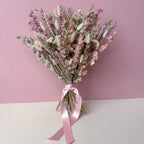 A dried flower bouquet with pink, white, and beige botanicals tied with a pink satin ribbon, set against a split pink and white background.
