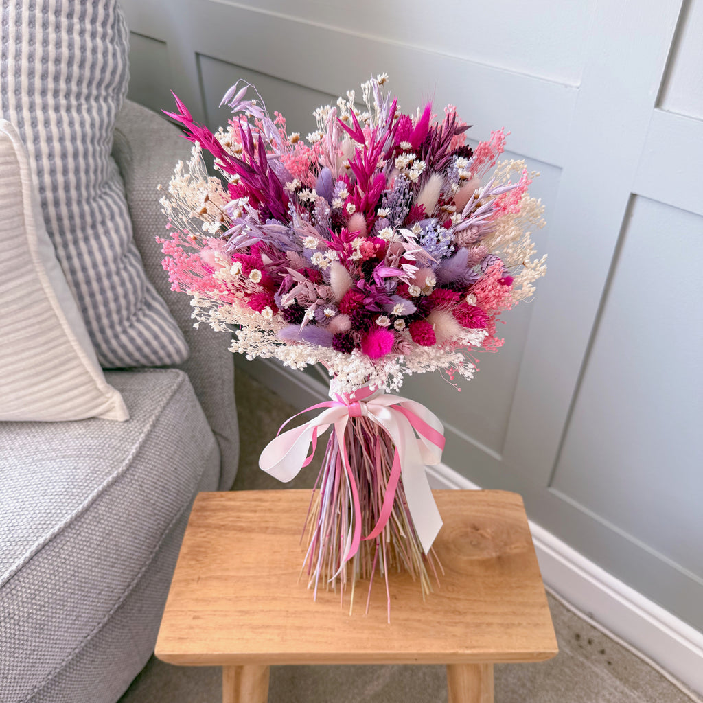 Bouquet of pink and purple flowers on a wooden table with a grey sofa in the background