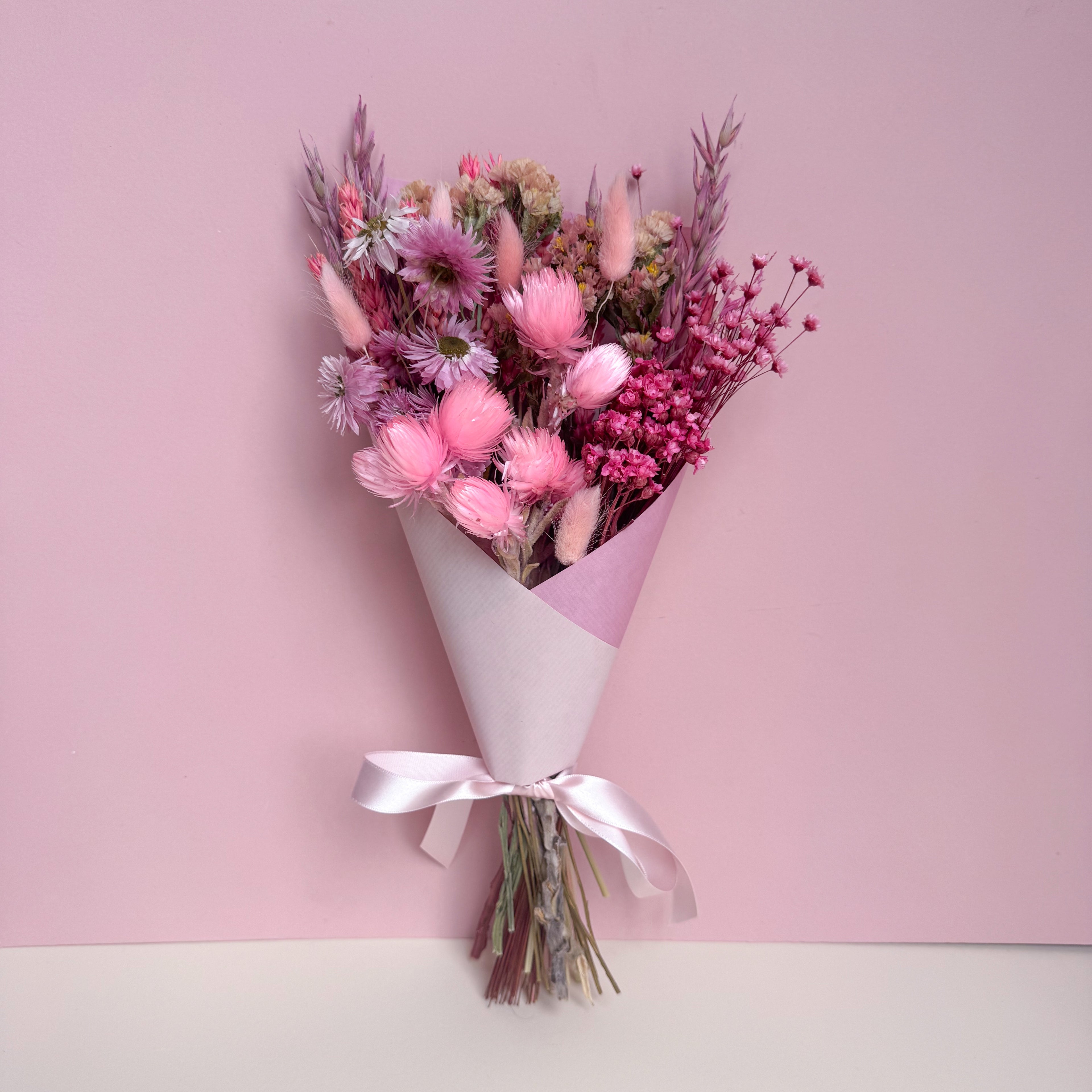 bouquet of pink dried flowers wrapped in pink paper and tied with a pink ribbon