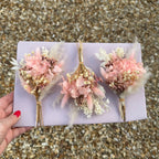 three buttonholes in pink colours with preserved pink hydrangea, pampas grass and cream babies breath