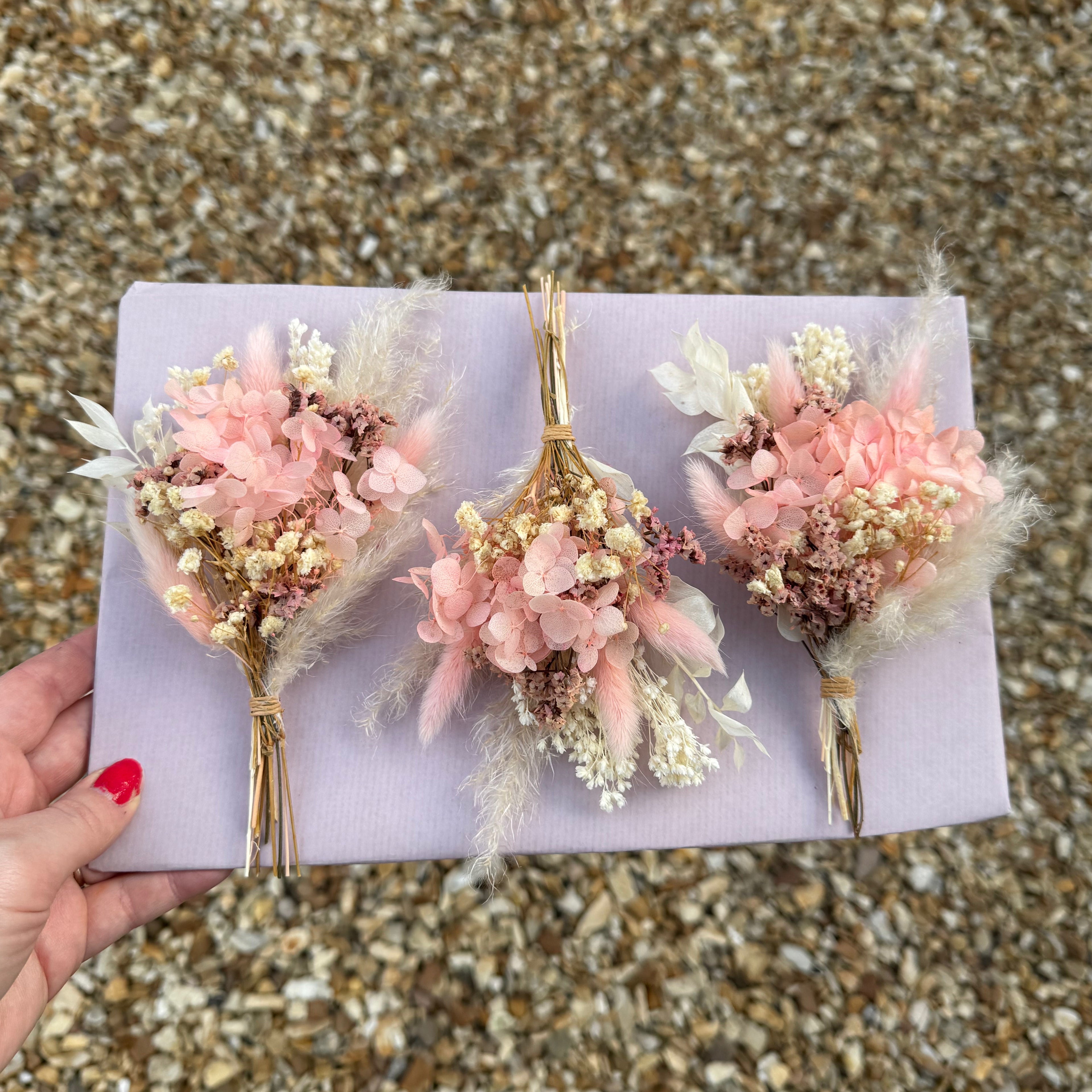 three buttonholes in pink colours with preserved pink hydrangea, pampas grass and cream babies breath