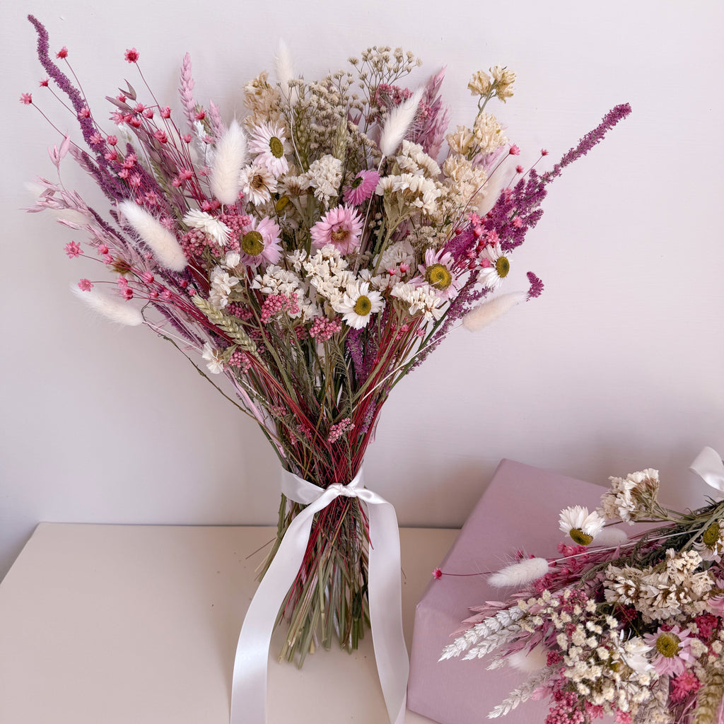 Bouquet of pink dried flowers with a white ribbon on a light surface.