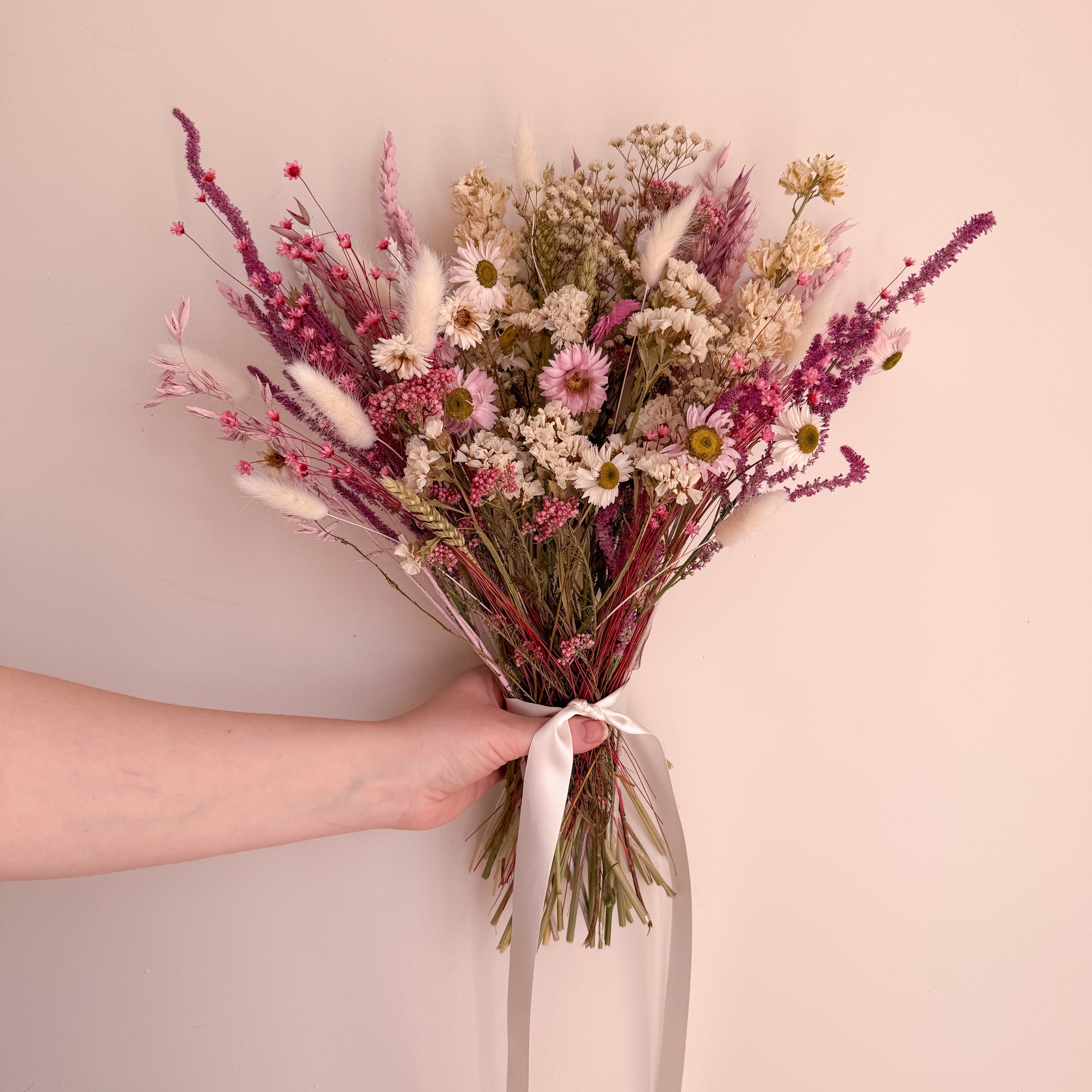 Bouquet of dried flowers held by a person against a plain background