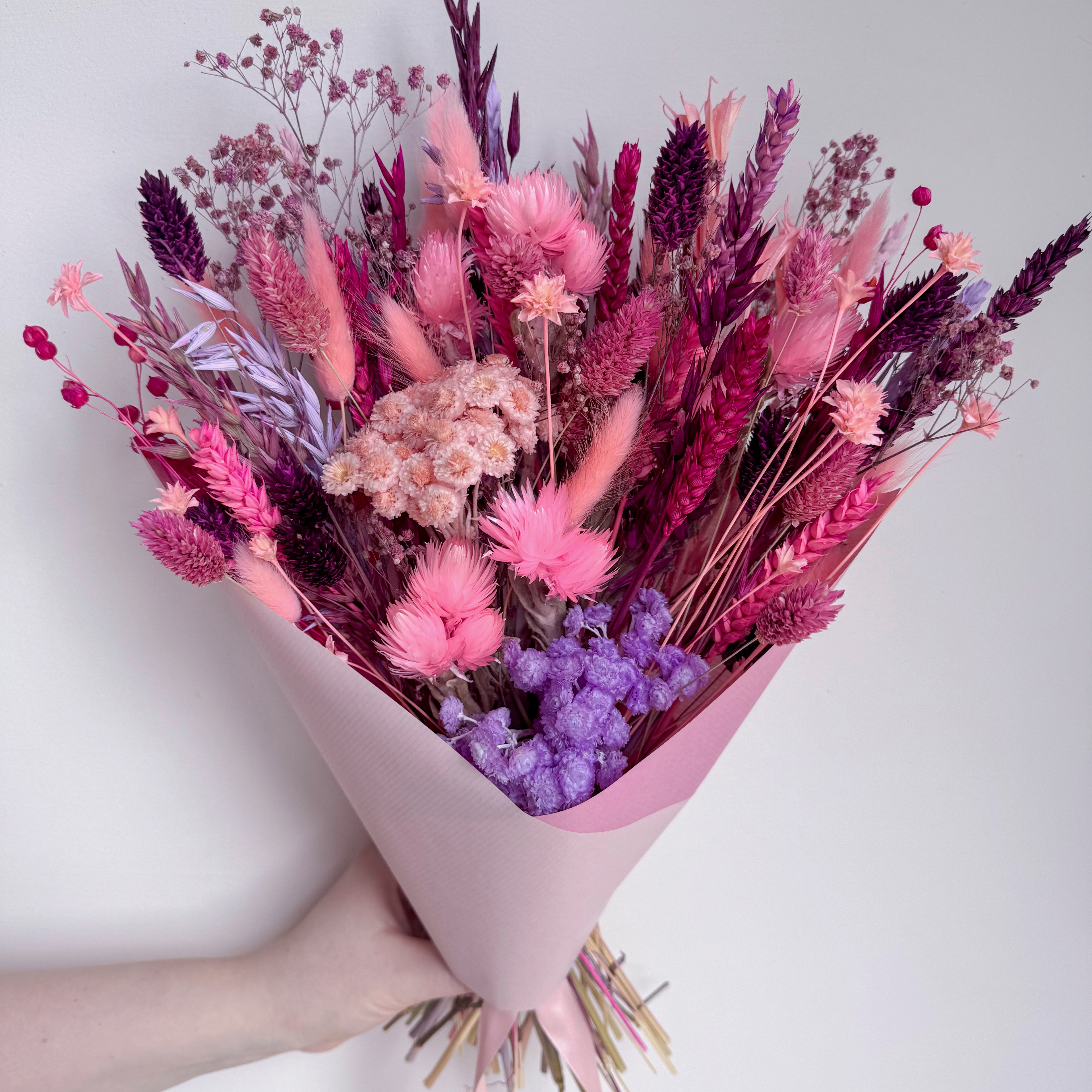 Bouquet of pink and purple flowers held by a hand against a white background