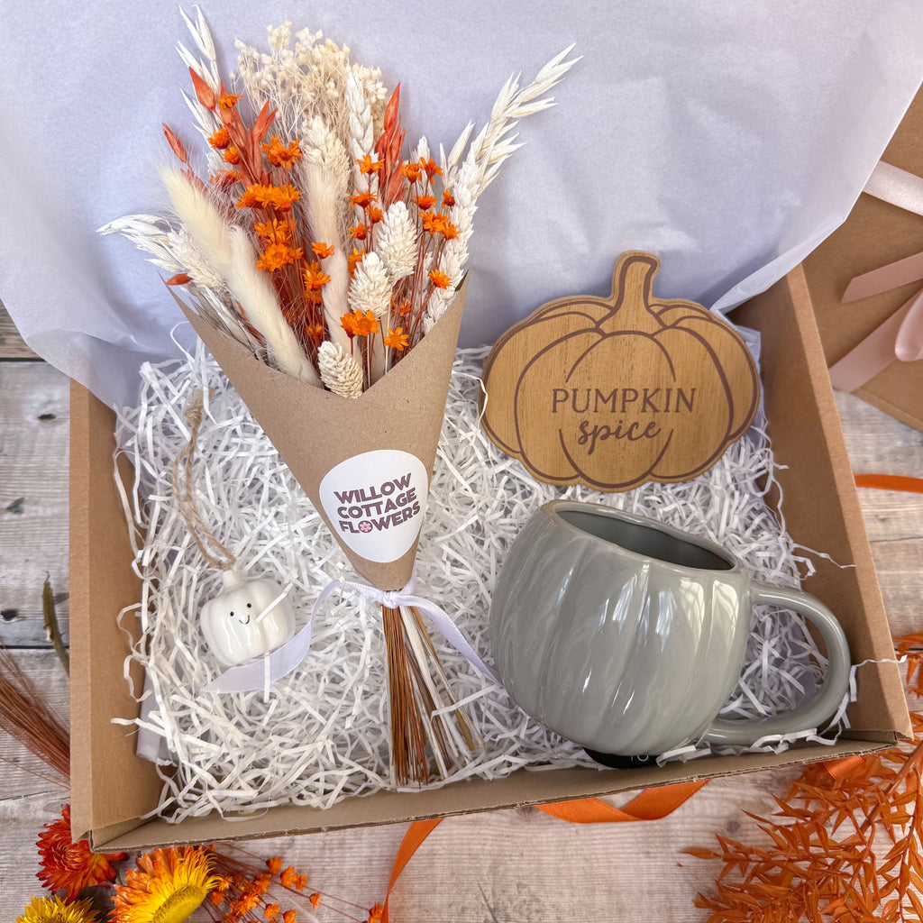 a pumpkin themed gift box containing orange and white dried flowers in brown paper gift wrap, pumpkin wooden coaster, mini hanging pumpkin decoration and grey pumpkin shaped mug