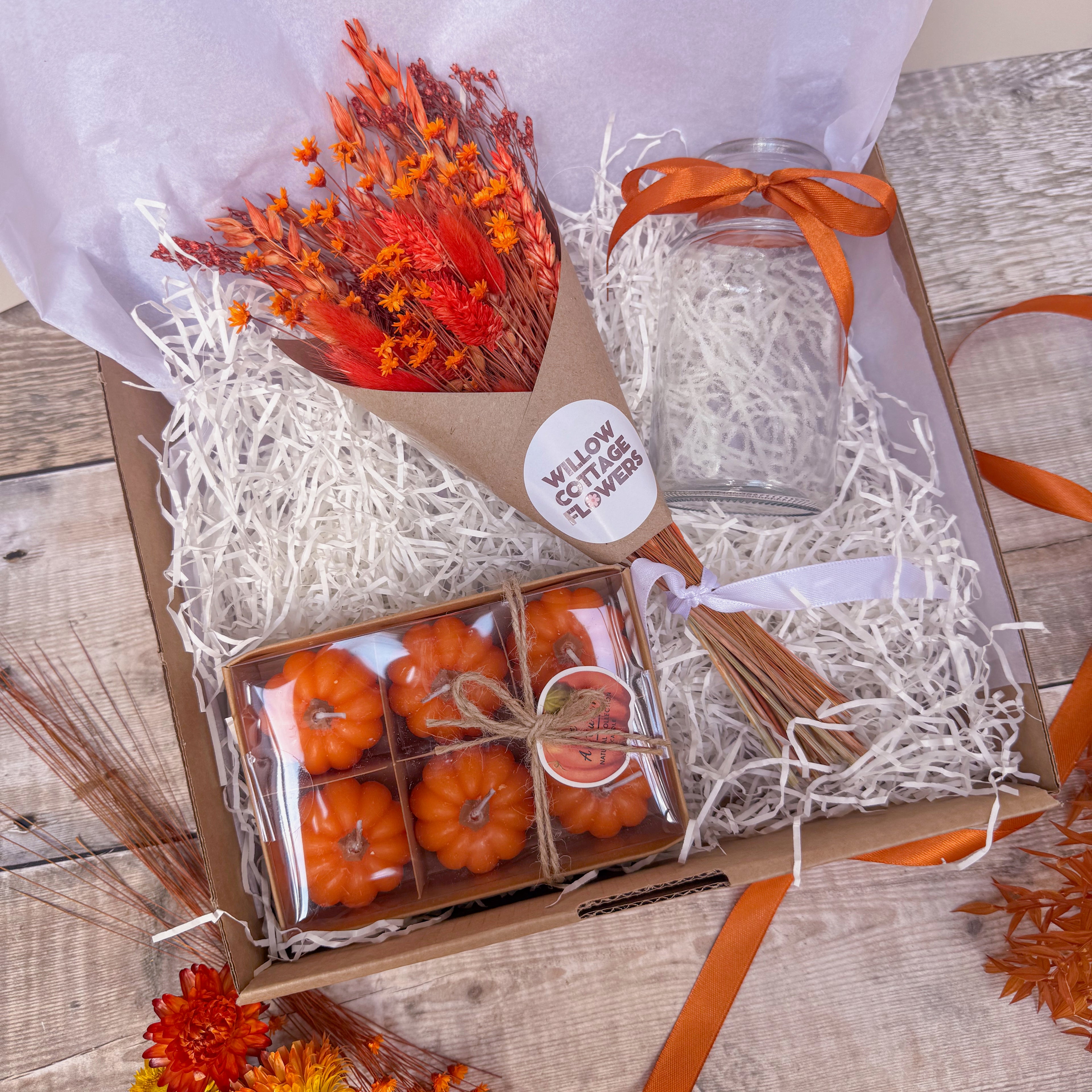 a pumpkin themed gift box with mini pumpkin candles, orange dried flowers and glass vase