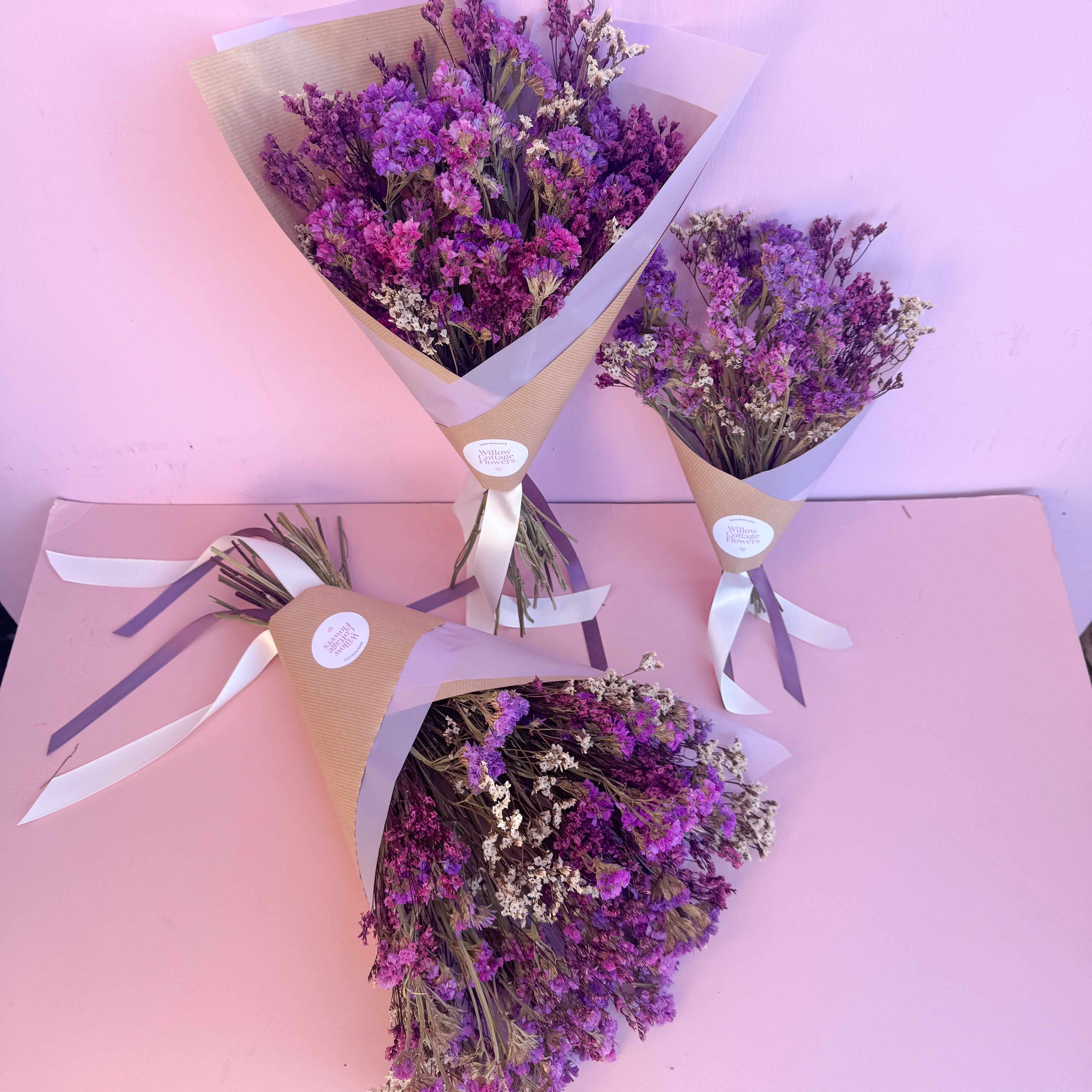 Three bouquets of purple statice flowers in paper gift packaging on a pink background