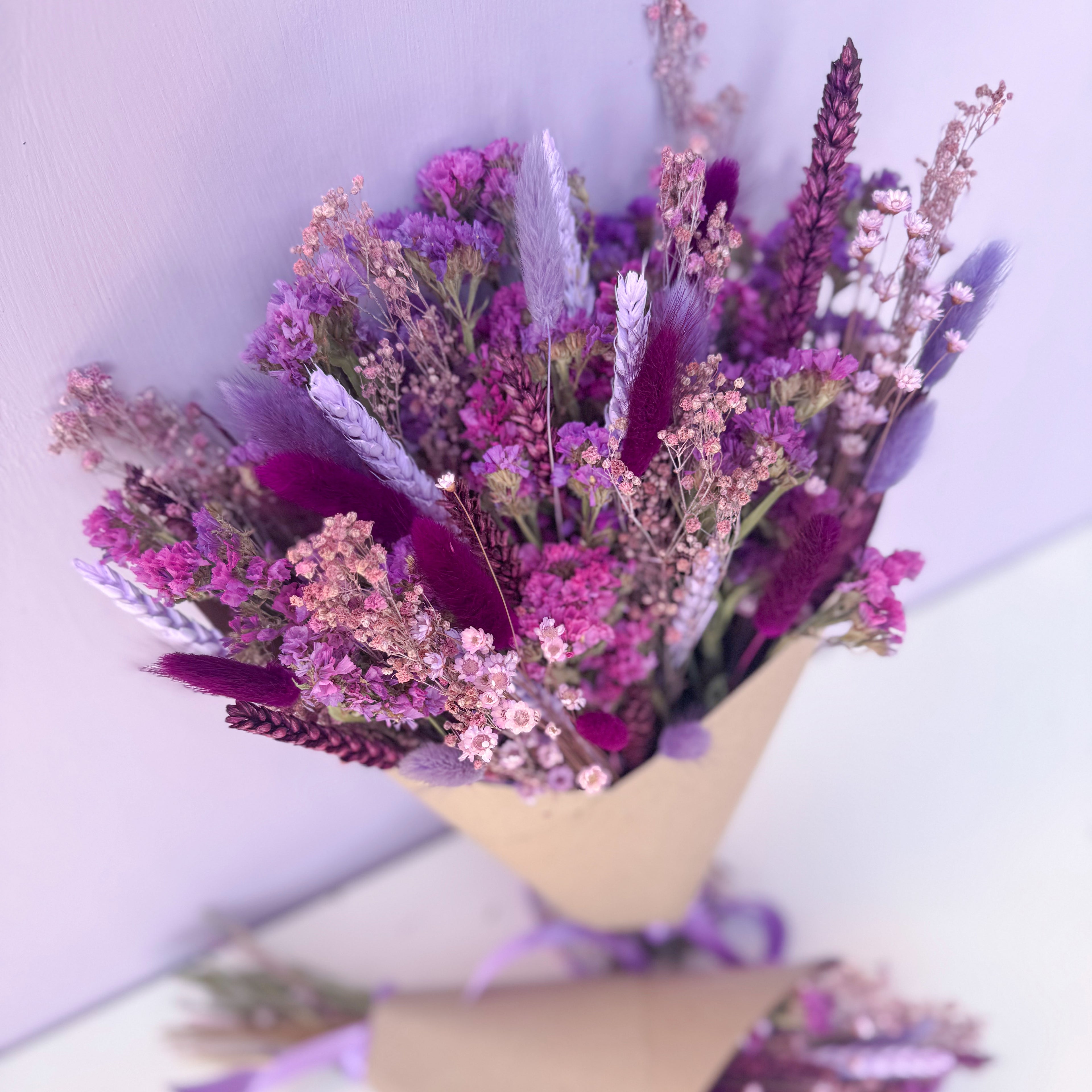 Bouquet of purple and pink flowers in gift wrap against a light purple background