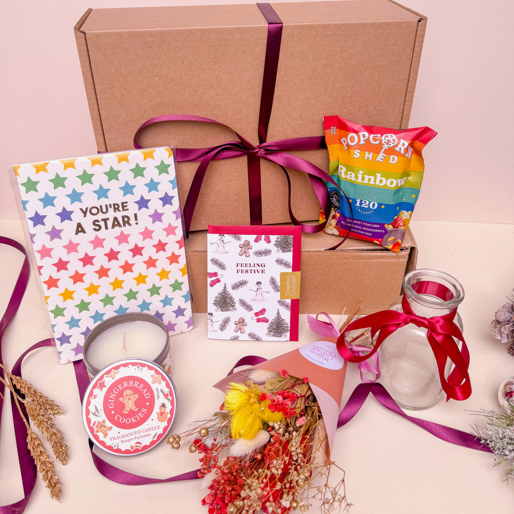 Christmas Gift box with stationery items, popcorn, and a candle on a light pink background