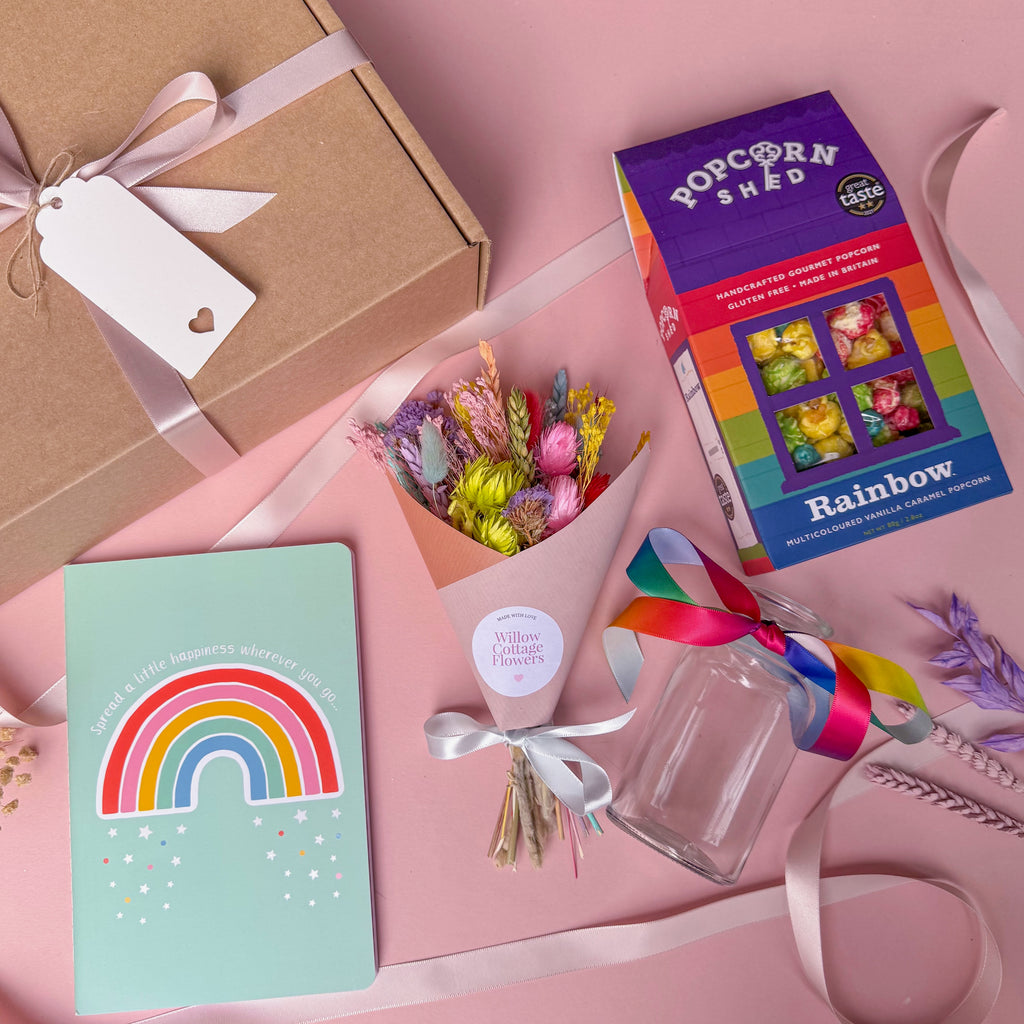 Gift set with a rainbow notebook, colourful dried flower bouquet and popcorn box on a pink background