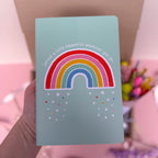 Light blue notebook with a rainbow design held by a hand against a blurred background