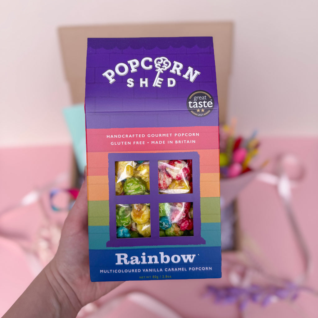 Box of Popcorn Shed Rainbow popcorn with colorful window design, held by a hand.