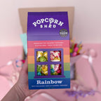 Box of Popcorn Shed Rainbow popcorn with colorful window design, held by a hand.