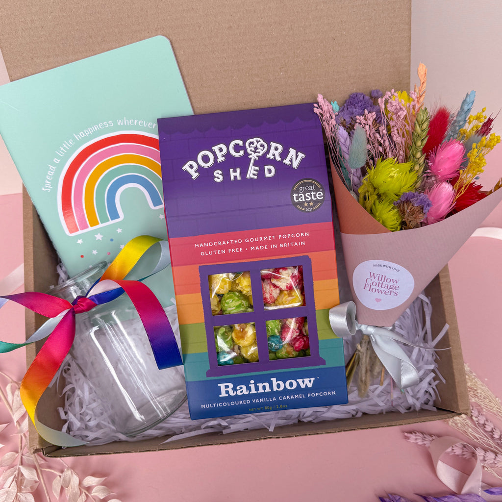 Gift box with rainbow popcorn, rainbow flowers, glass vase with rainbow ribbon and a notebook.