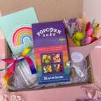 Gift box with rainbow popcorn, rainbow flowers, glass vase with rainbow ribbon and a notebook.