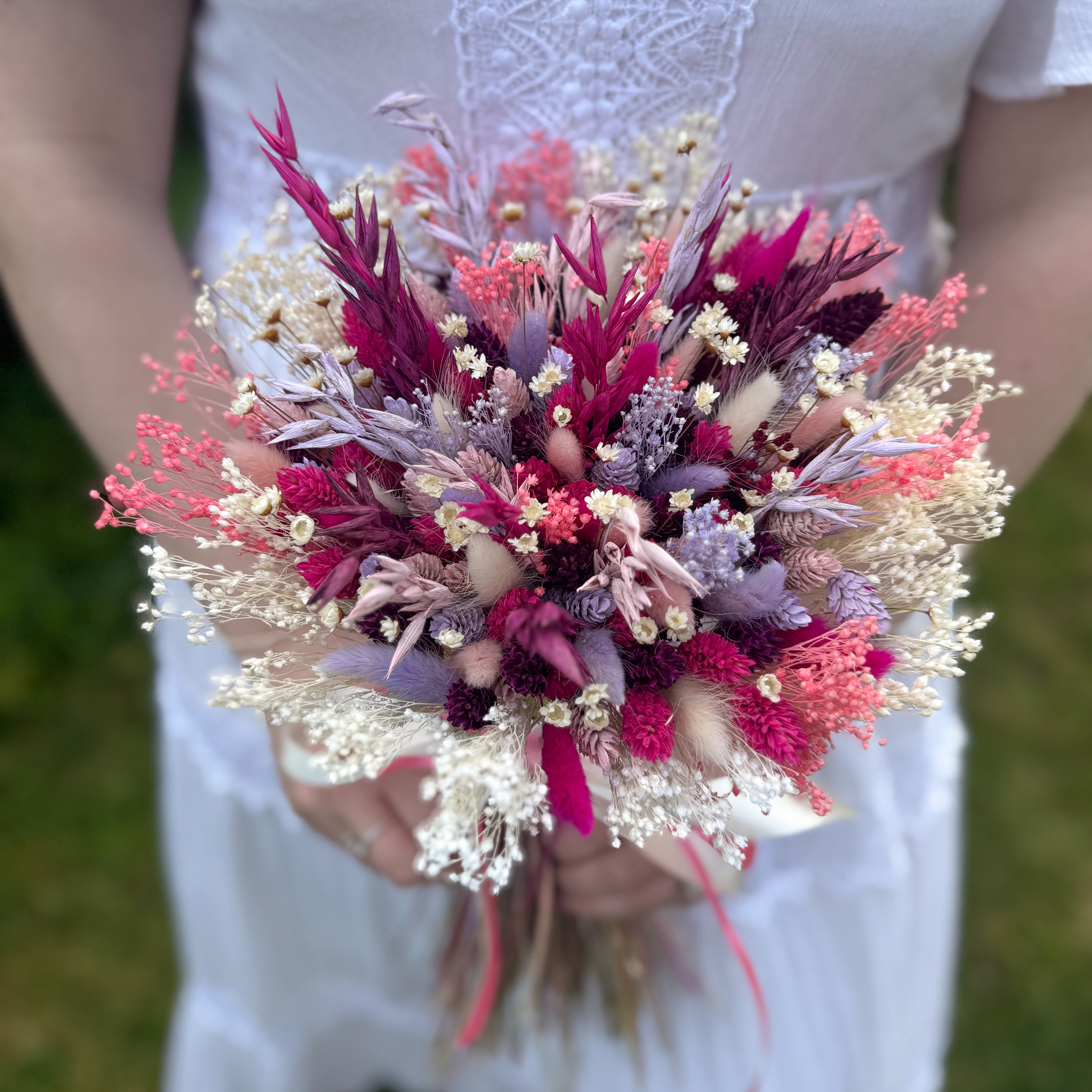 Bouquet of dried flowers held by a person wearing a white dress.