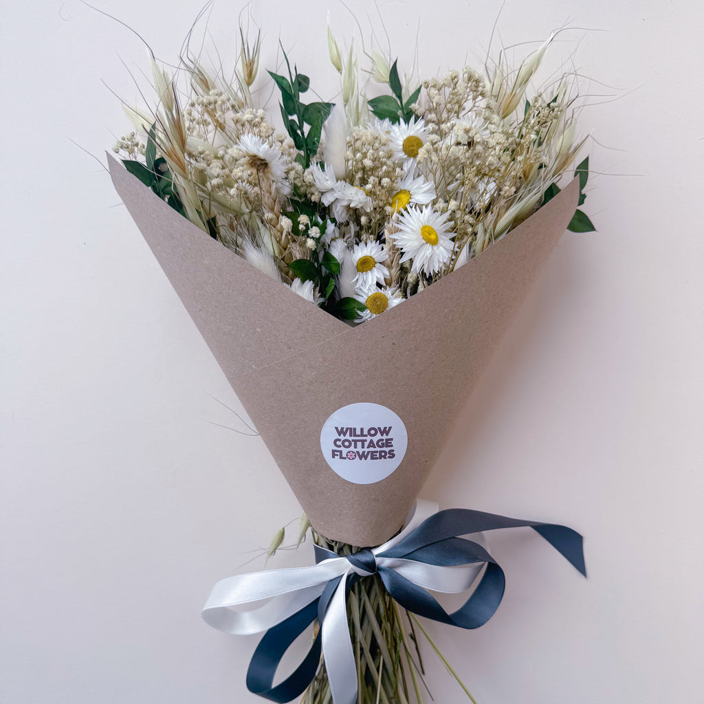 a rustic daisy arrangement in green and white, wrapped in a brown paper wrap and tied with a white and dark green ribbon