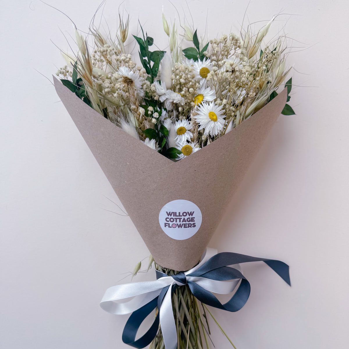 a rustic daisy arrangement in green and white, wrapped in a brown paper wrap and tied with a white and dark green ribbon