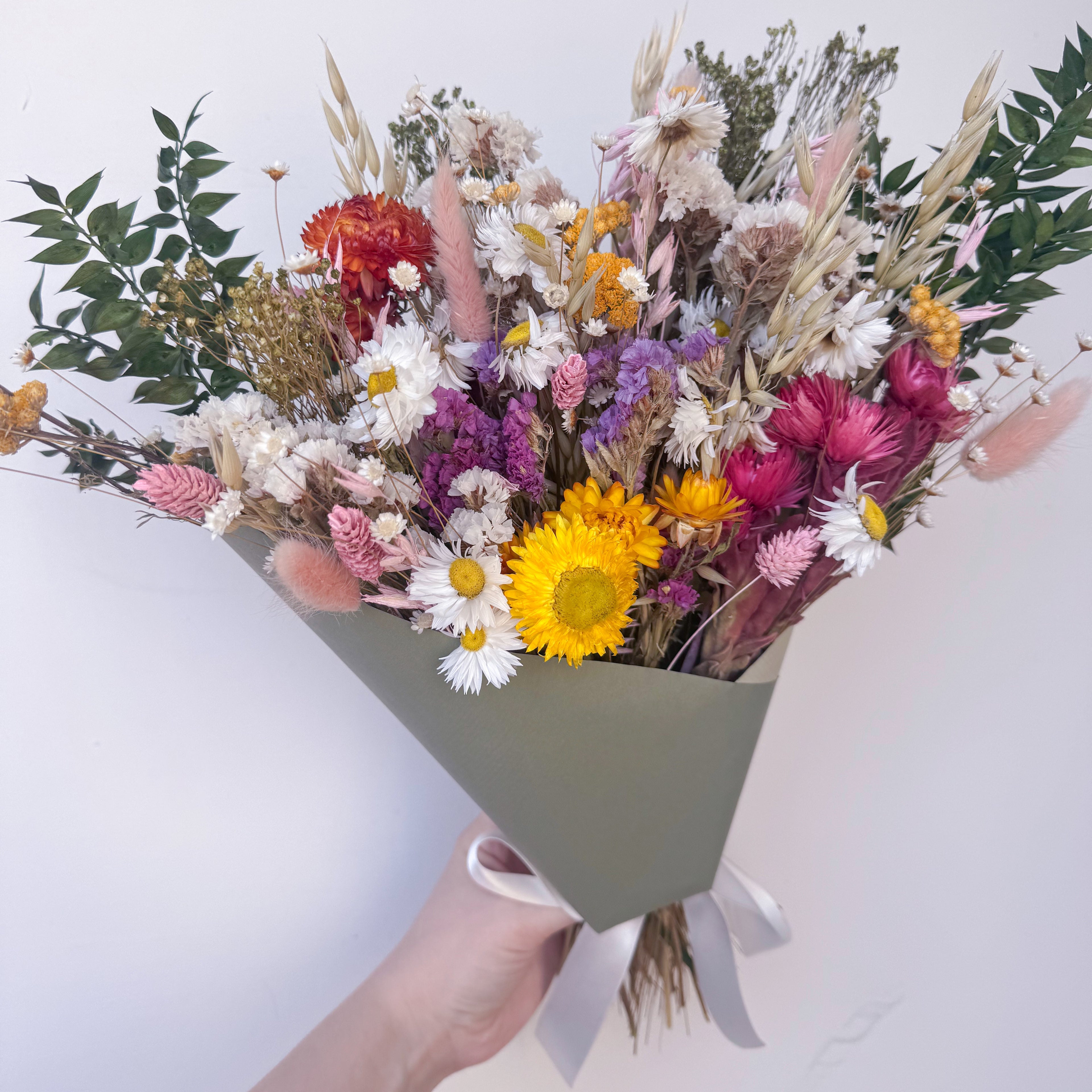 a colourful dried flower bouquet with green ruscus in green gift wrap