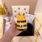 Hand holding a bee themed vase with a gift box in the background