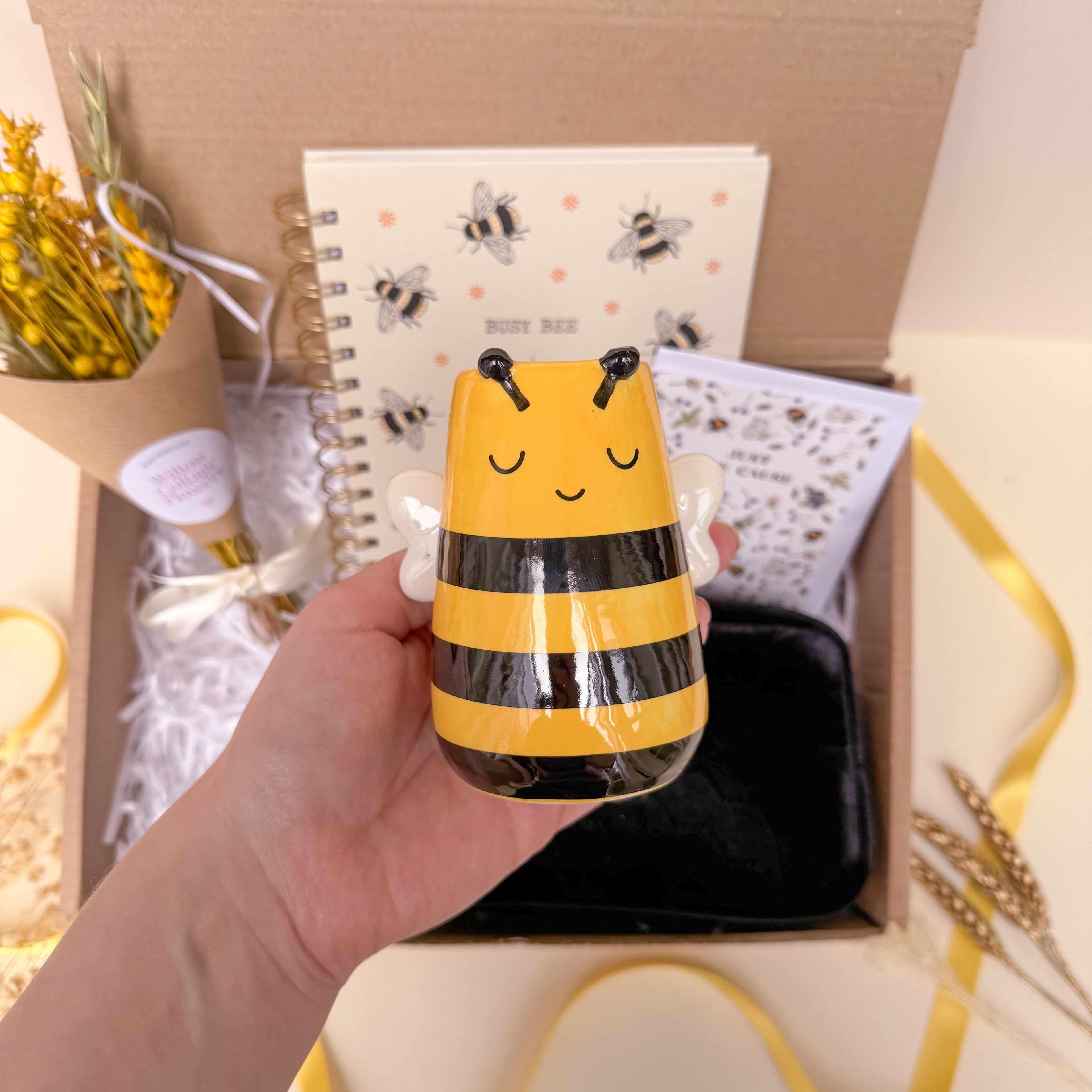 Hand holding a bee themed vase with a gift box in the background