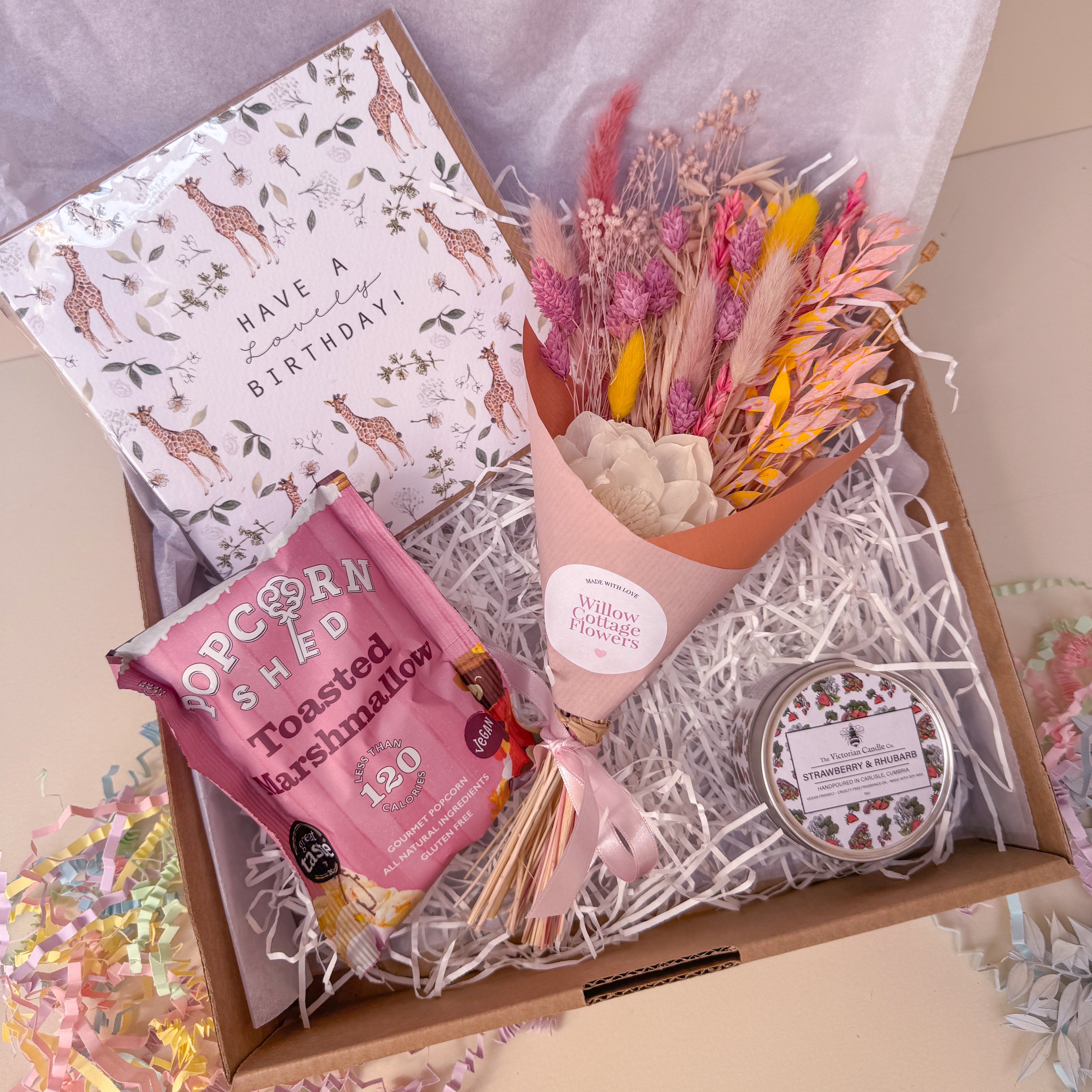 Gift box with flowers, popcorn, and a card on a light background