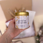 Hand holding a candle tin labeled 'Sparkling Snowflakes' with a blurred background