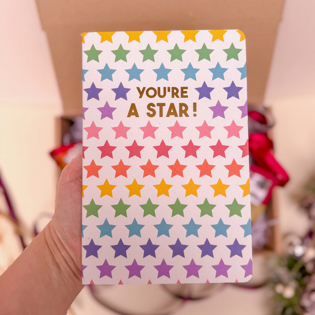 Notebook with colorful star pattern and 'You're a Star!' text held by a hand.