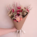 Bouquet of daisy flowers wrapped in brown paper held by a hand against a light pink background