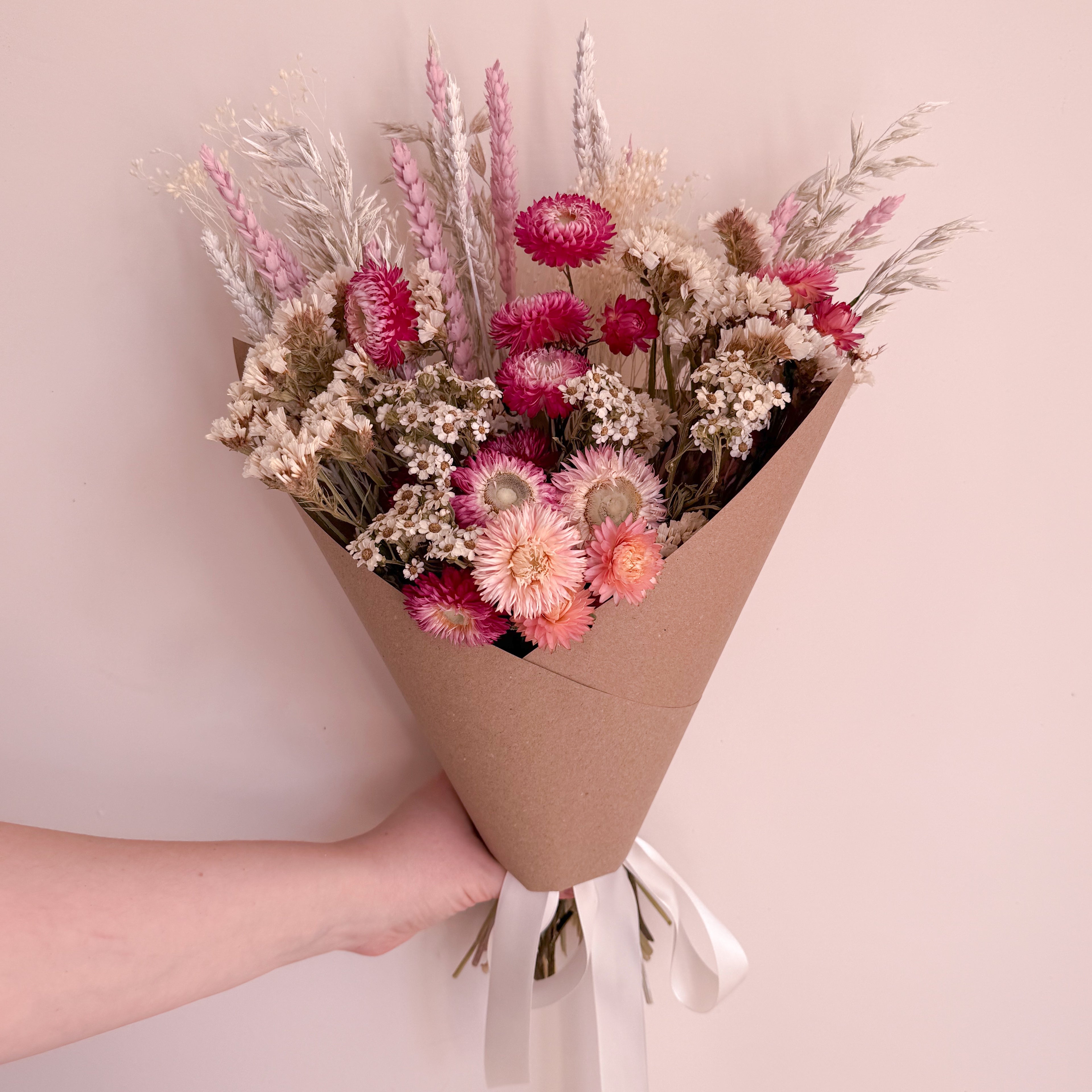 Bouquet of daisy flowers wrapped in brown paper held by a hand against a light pink background
