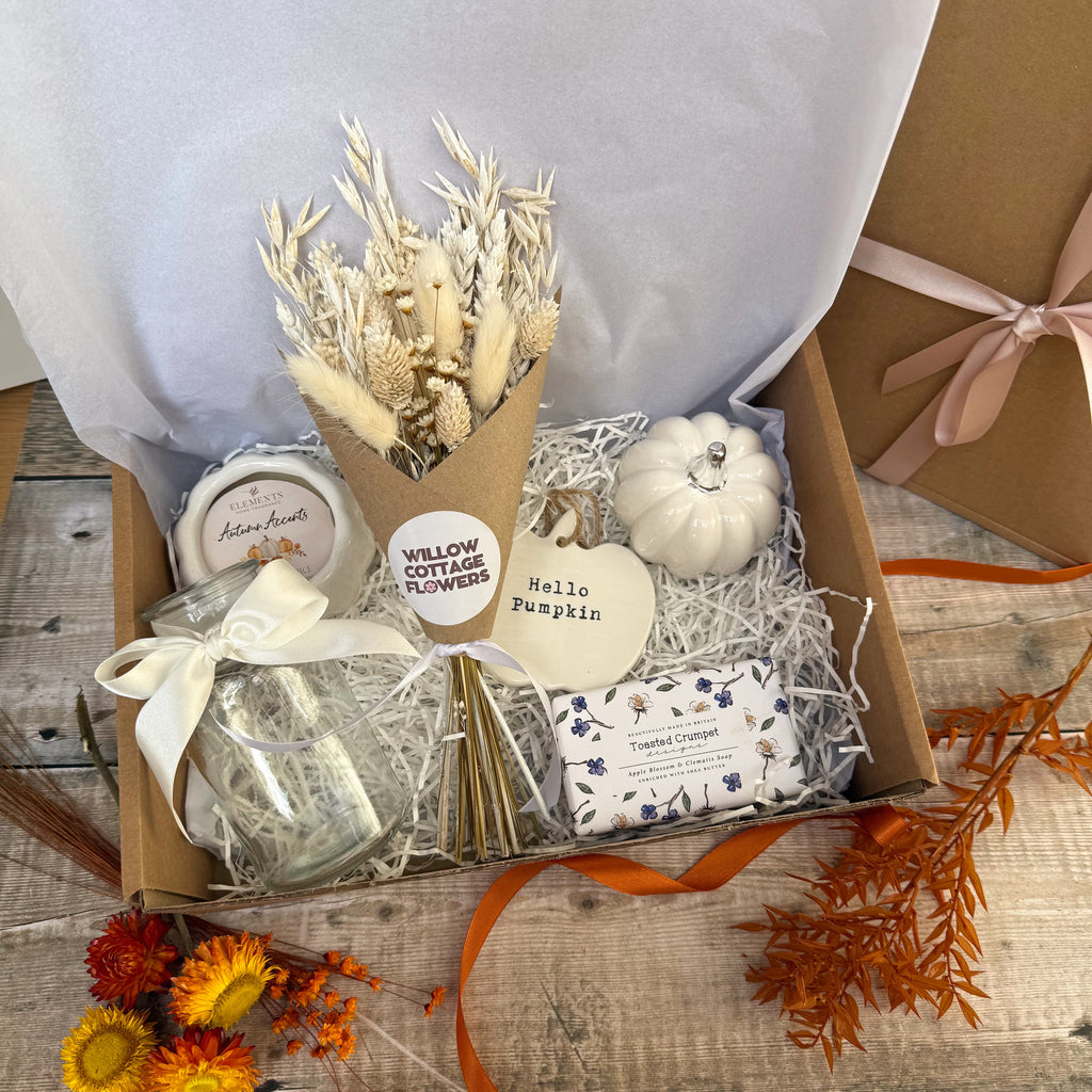 an autumn themed gift box in white. includes products such as dried flowers, candle, soap, vase, pumpkin ornament and hanging pumpkin decoration