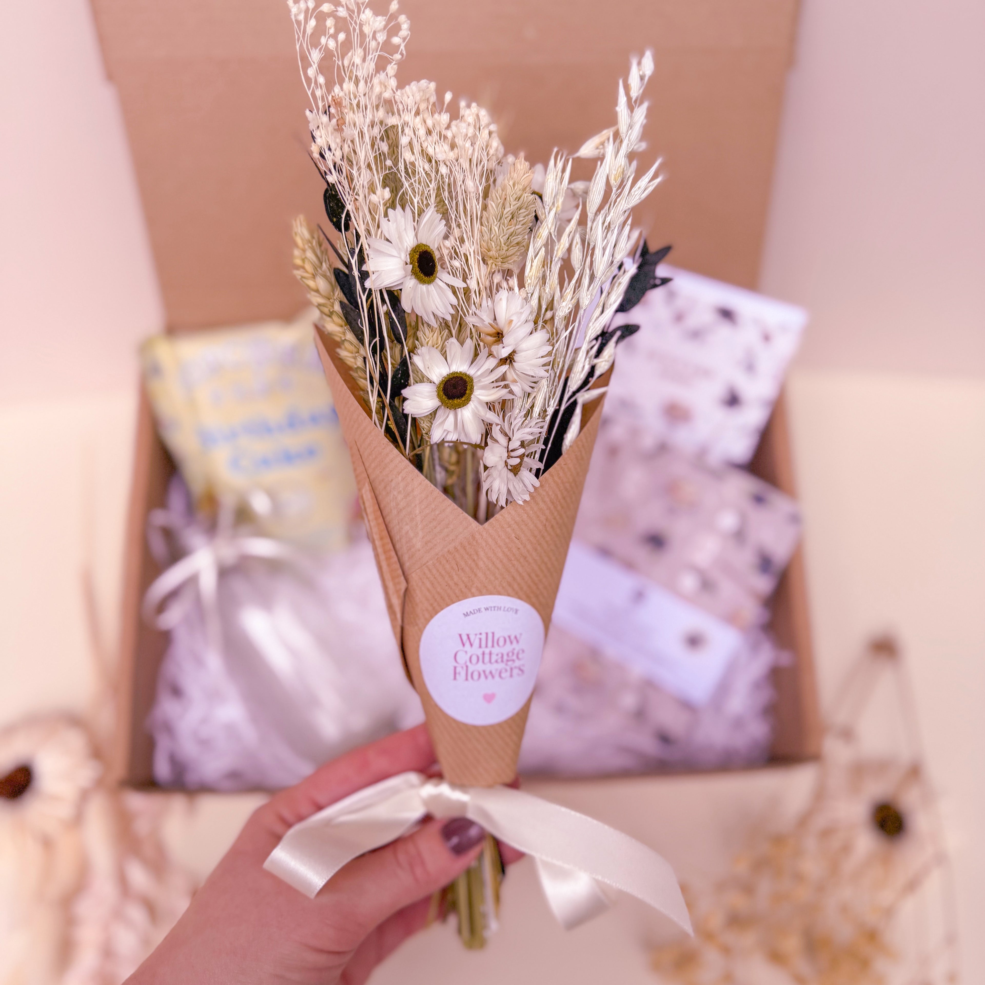 Bouquet of dried flowers in a brown paper cone held by a hand with a blurred background.