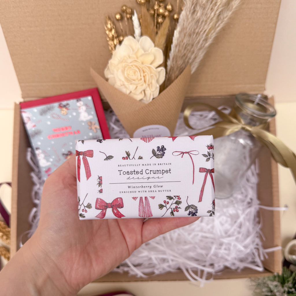 Hand holding a bar of soap with decorative bow packaging in front of a gift box.